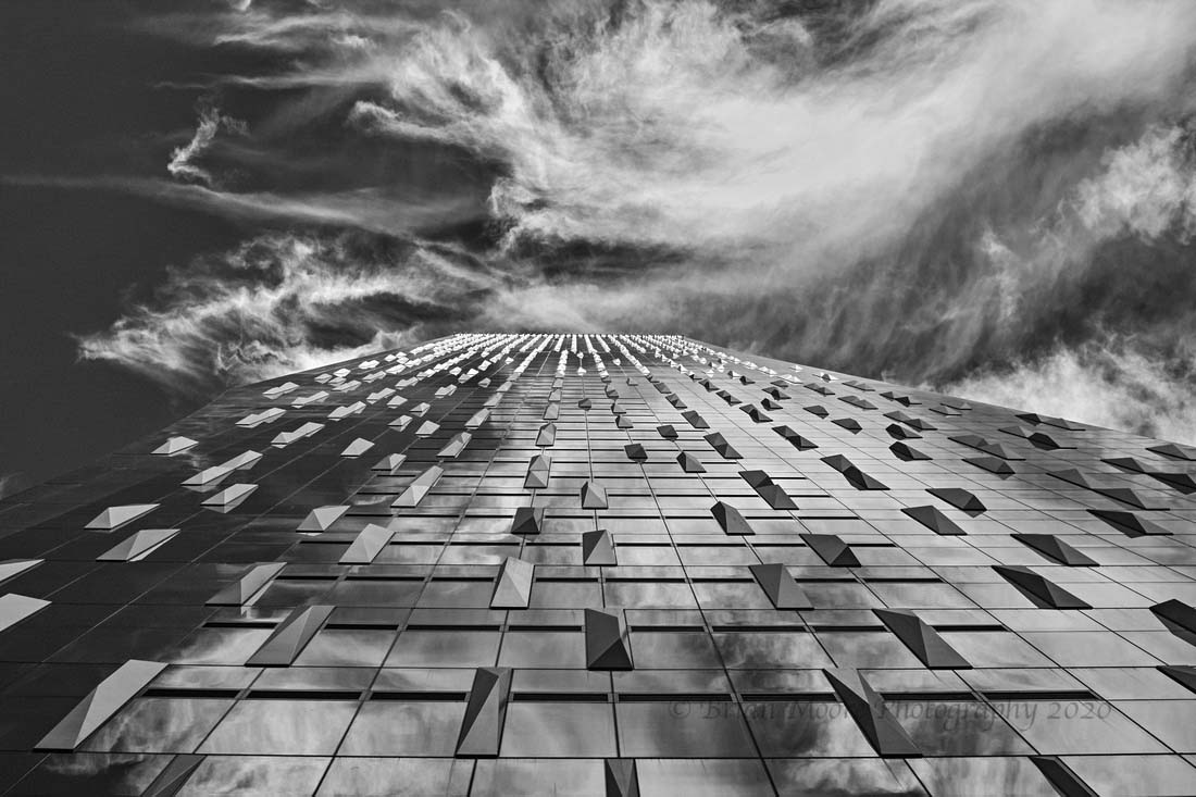 Upward view of Rainier Square tower's geometric curtainwall facade against dramatic cloudy sky